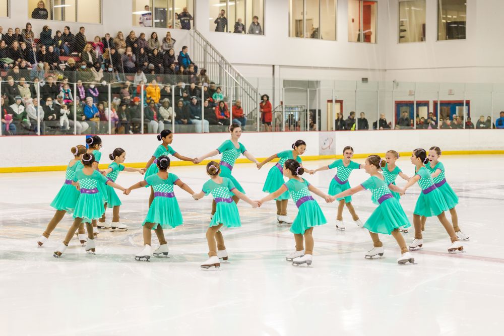 Aspire 2 synchronized skating team on ice in teal costumes performing.