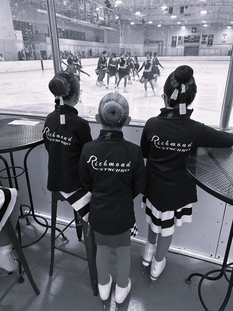a black and white photo of younger synchro skates watching the older team